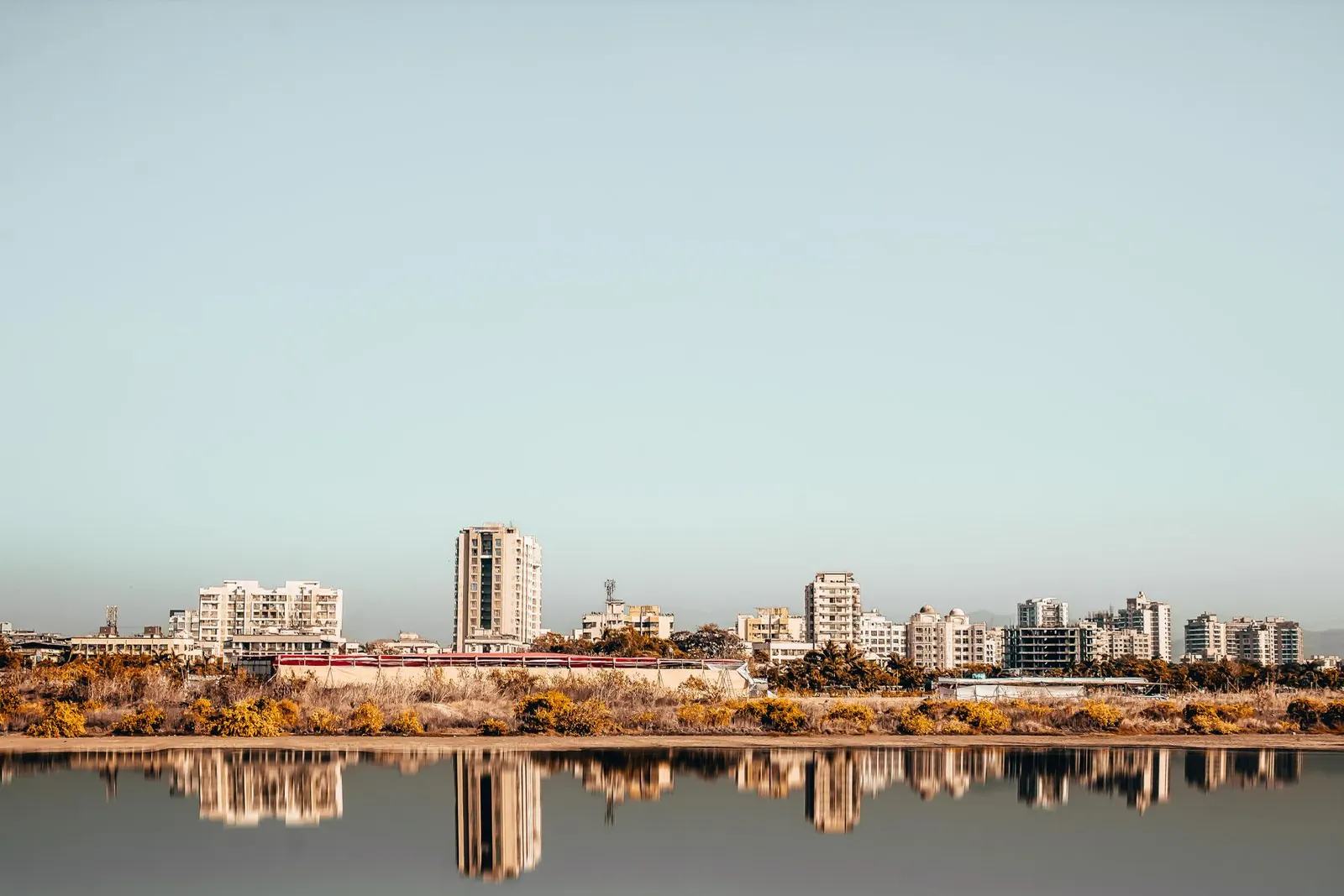 A flat city skyline reflected in still water under a pale sky