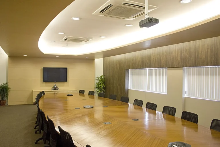 An empty boardroom with a long wooden table, leather chairs and a wall screen