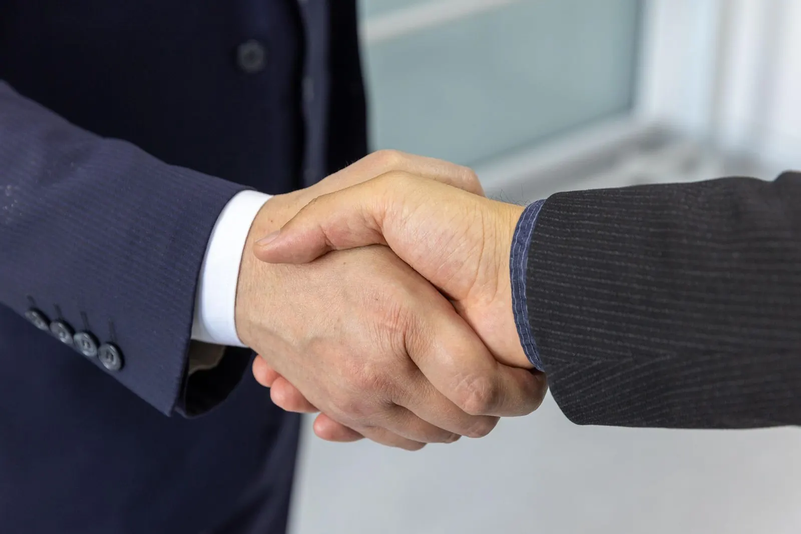 Two business people in suits shaking hands, close up