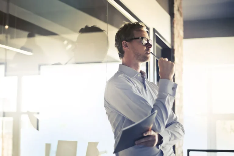 A business leader standing in a bright office, thinking, with a tablet and pen