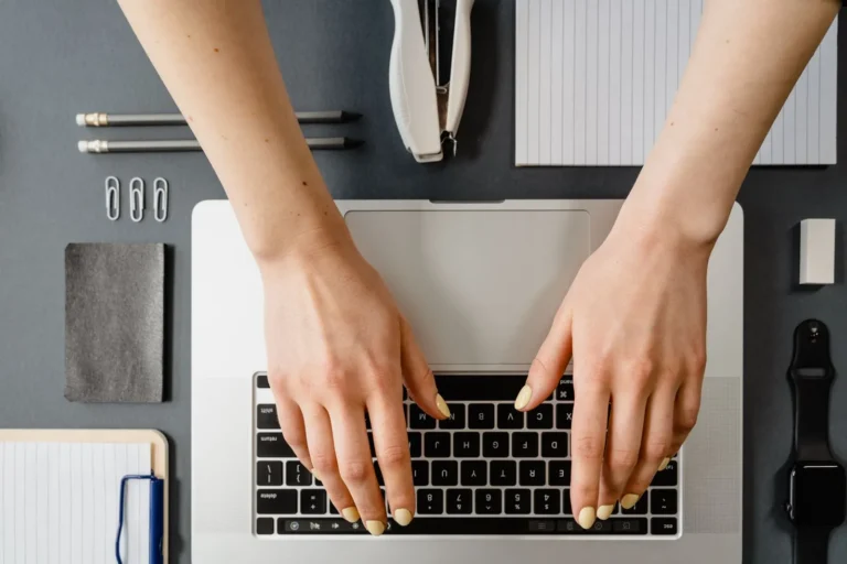 Hands typing on a laptop keyboard on a desk, seen from above
